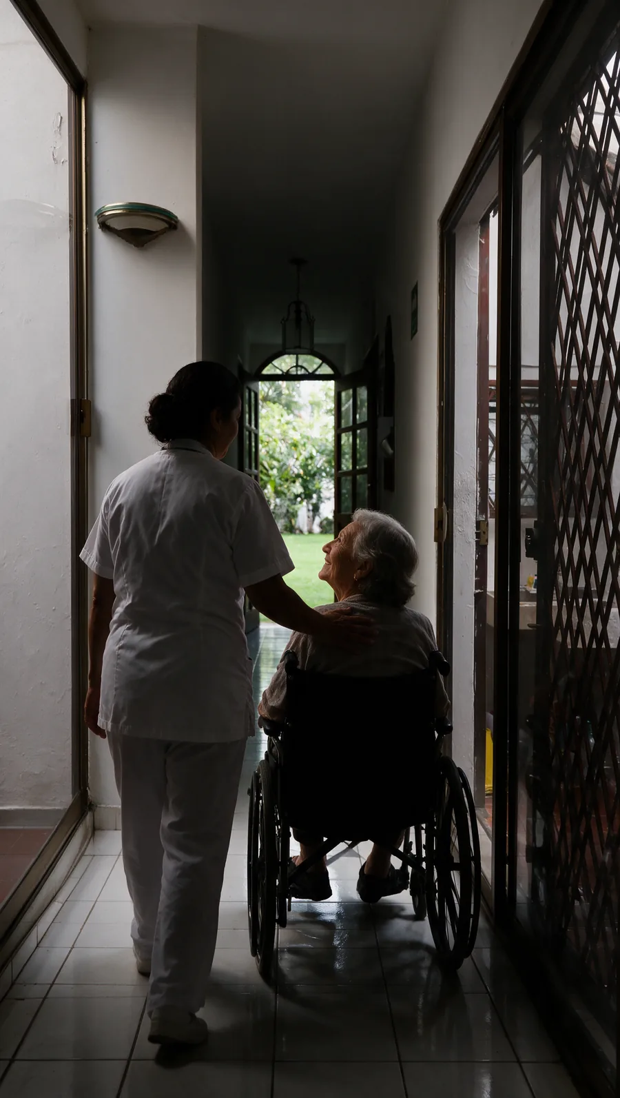 Cuidadora acompañando a una residente en silla de ruedas hacia el jardín